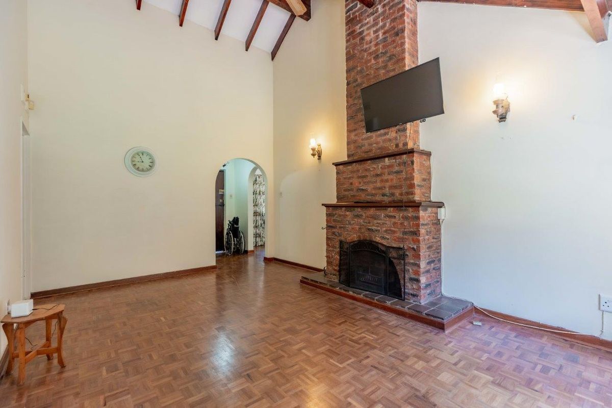 Spacious living room featuring a prominent brick fireplace, high vaulted ceilings with exposed timber beams, and classic parquet flooring.
