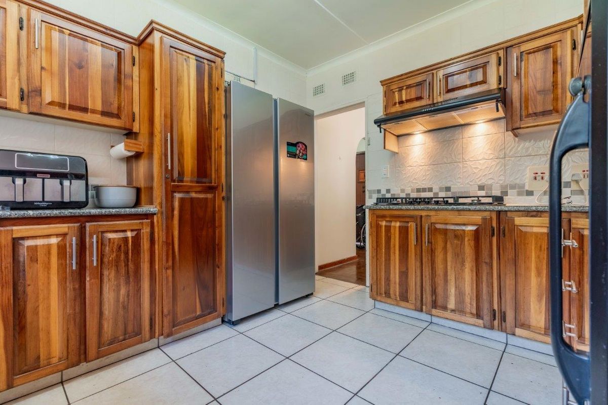A functional kitchen featuring warm-toned wooden cabinetry, granite countertops, a gas hob with an extractor fan, and tiled flooring.