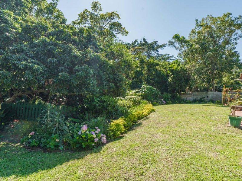 A well-maintained garden featuring a lush green lawn, mature trees, established garden beds, and a paved patio area for outdoor relaxation.