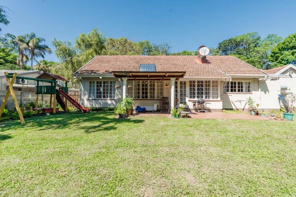 Rear view of the house featuring a spacious lawn, a covered patio area with wooden columns, and a tiled roof with solar water heating.