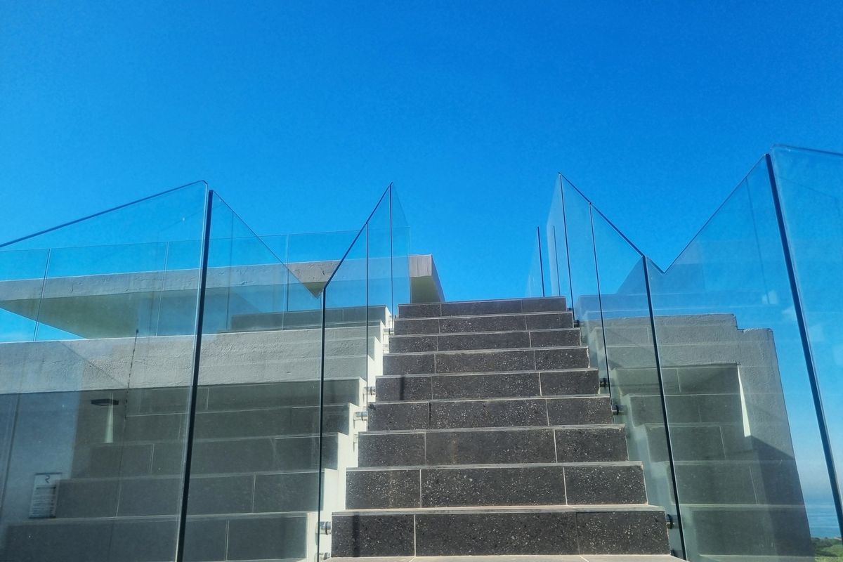 Modern exterior staircase featuring dark stone steps and frameless glass balustrades leading to an upper level.