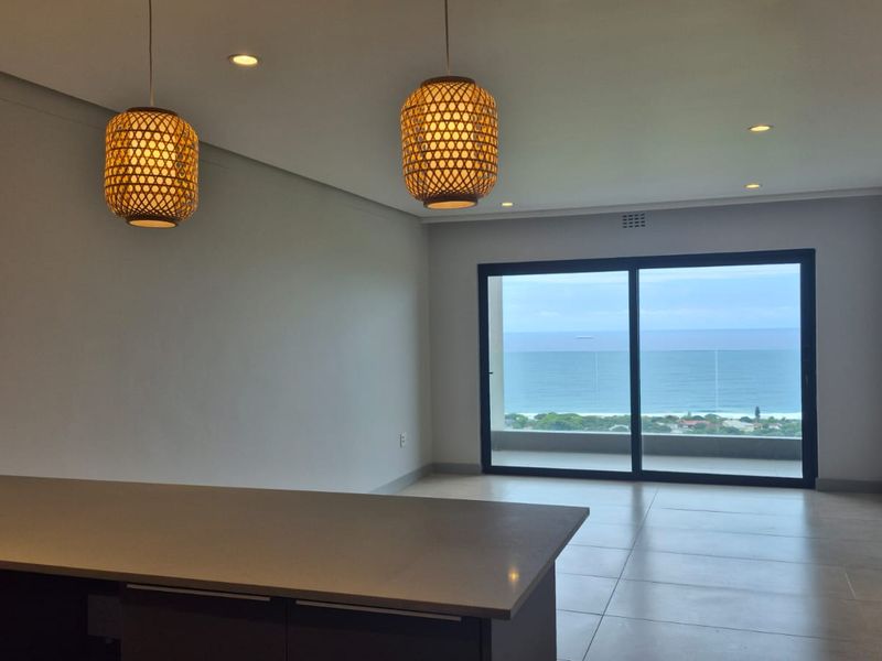 Spacious open-plan living area featuring modern tiled floors, recessed lighting, and a large sliding glass door offering expansive ocean views.
