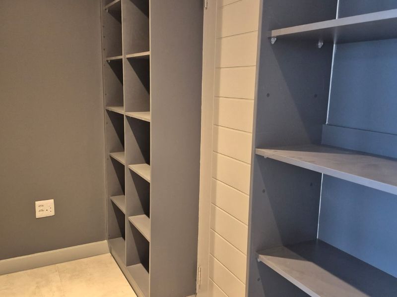 A clean, modern walk-in closet or bedroom storage area featuring built-in grey shelving units and neutral tiled flooring.