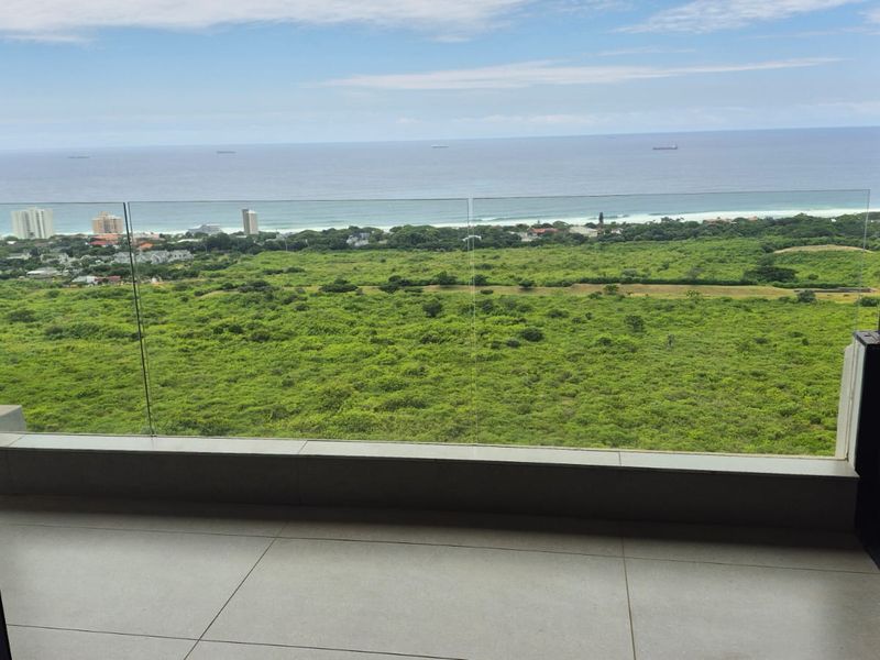 A modern balcony featuring a frameless glass balustrade and tiled flooring, offering expansive views of the surrounding landscape and coastline.