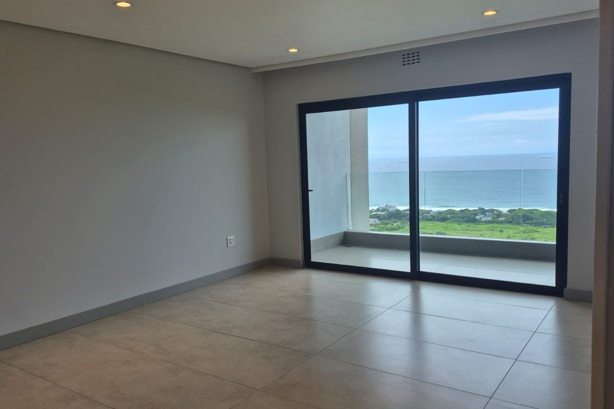 A bright, empty living area featuring large sliding glass doors that open onto a balcony with expansive ocean views.
