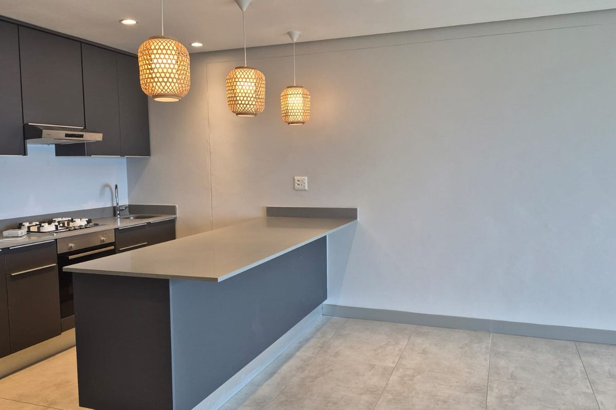 Modern kitchen featuring dark grey cabinetry, stone countertops, a breakfast bar, and integrated stainless steel appliances, finished with neutral floor tiles.