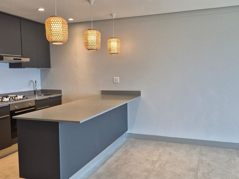 Modern kitchen featuring dark grey cabinetry, stone countertops, a breakfast bar, and integrated stainless steel appliances, finished with neutral floor tiles.