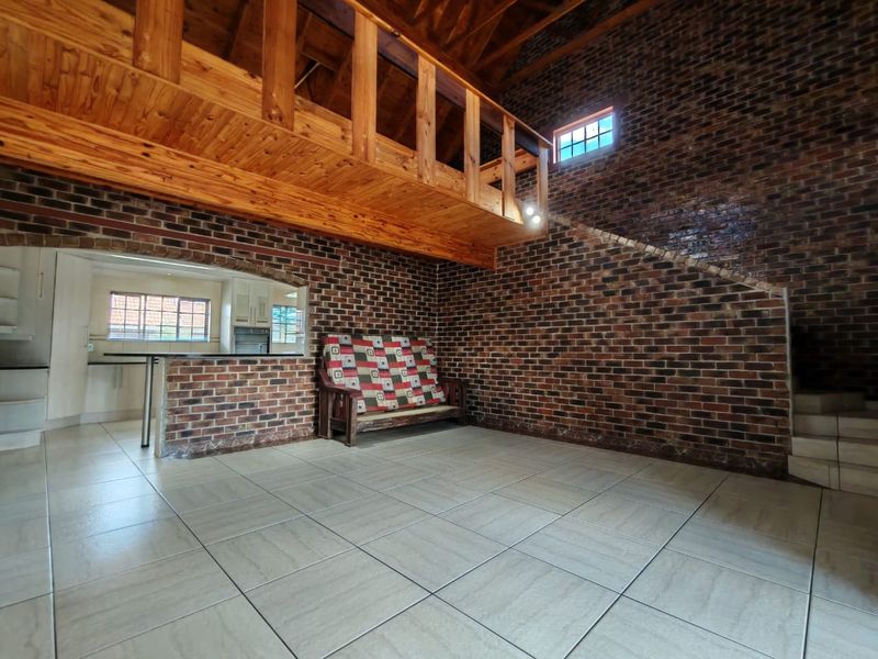 Spacious open-plan living area featuring rustic exposed brick walls, a timber mezzanine loft, and a breakfast bar connecting to the kitchen.