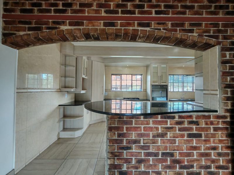 Spacious kitchen featuring a distinctive exposed brick archway, granite breakfast bar, built-in oven, gas hob, and ample fitted cabinetry with neutral tiled finishes.