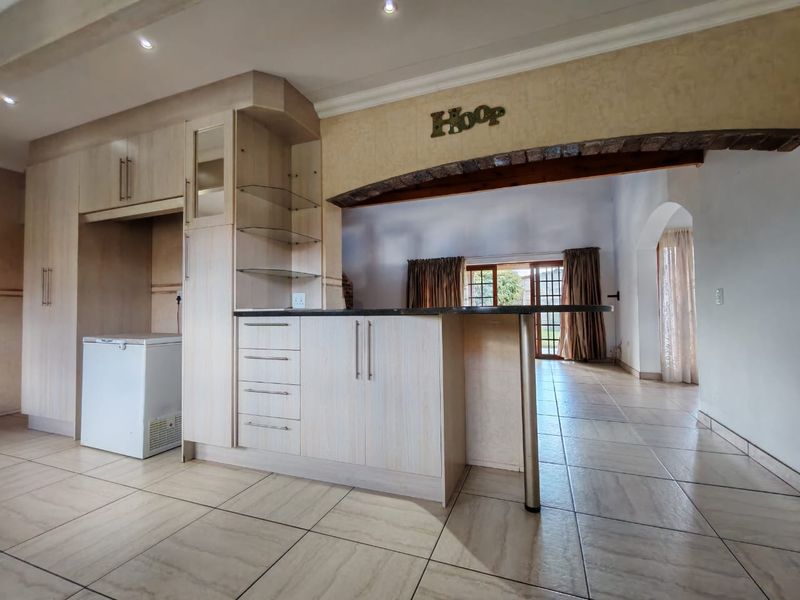 Open plan kitchen area featuring light wood cabinetry, granite breakfast bar, and tiled flooring, seamlessly connecting to the adjacent living space through a brick archway.