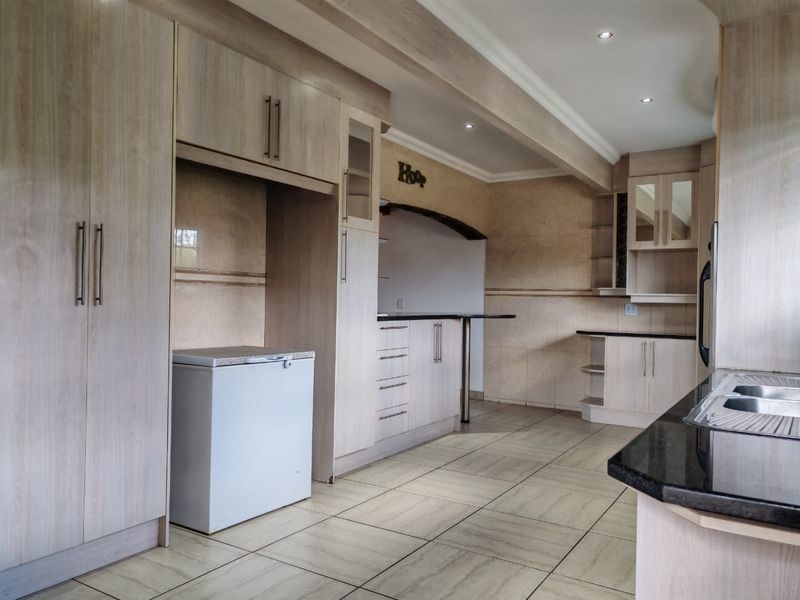 A spacious kitchen featuring light wood-finish cabinetry, granite countertops, a double bowl sink, and tiled flooring, offering a clean and functional layout.
