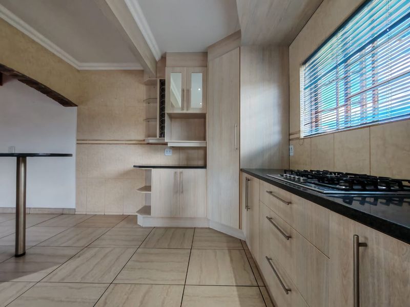 A modern kitchen featuring light wood-finish cabinetry, granite countertops, a built-in gas hob, and neutral tiled flooring throughout.