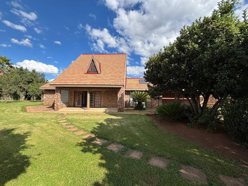 Rear view of a brick farmhouse featuring a covered patio, tiled roof with a dormer window, and a well-maintained garden with a stone walkway.