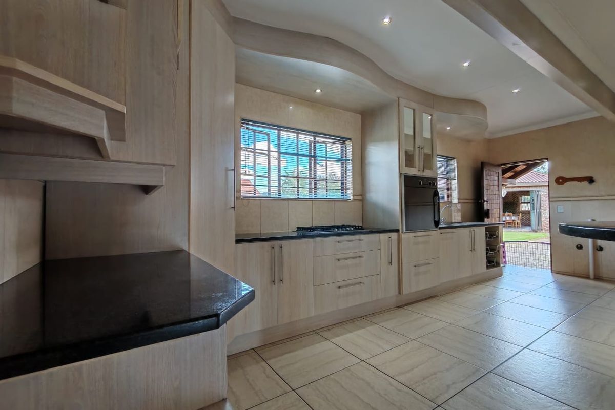 Spacious kitchen featuring light wood cabinetry, granite countertops, integrated oven, gas hob, and tiled flooring with direct access to the outdoor patio area.