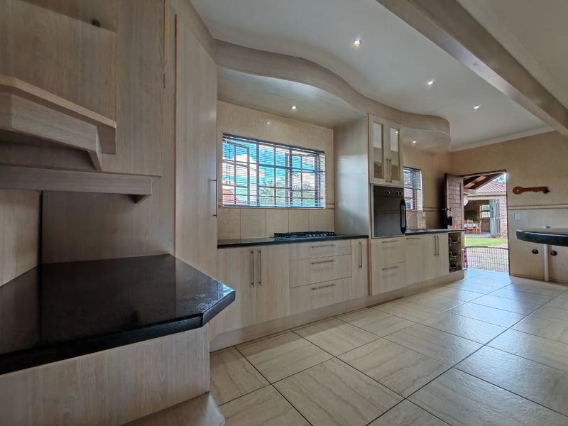Spacious kitchen featuring light wood cabinetry, granite countertops, integrated oven, gas hob, and tiled flooring with direct access to the outdoor patio area.