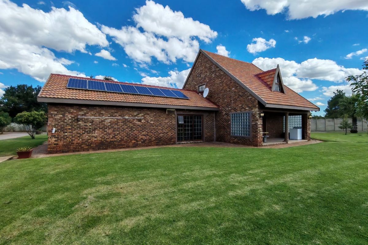 Rear view of a facebrick farm-style residence featuring a terracotta tiled roof, integrated solar panels, and a covered patio area set within a lawn.