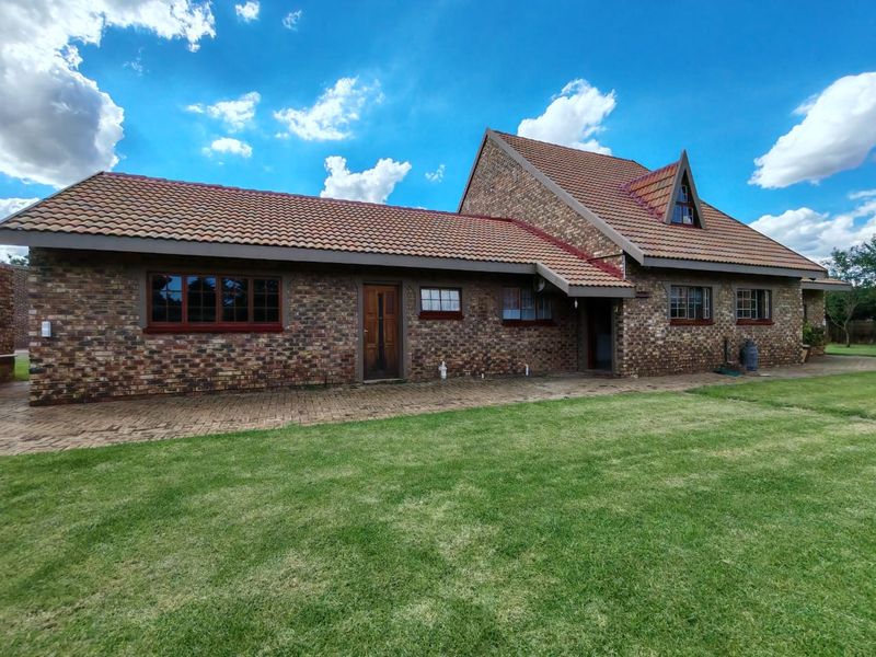 A well-maintained face-brick farmhouse exterior featuring a tiled roof, paved patio area, and established lawn, showcasing classic architectural character.