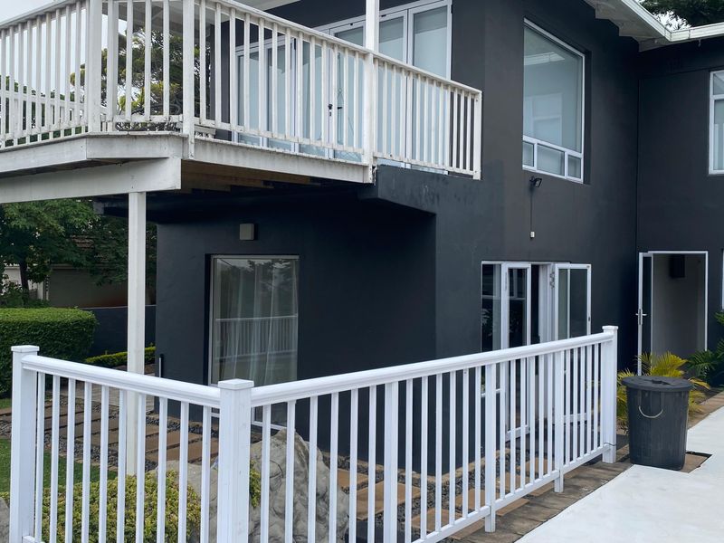 Rear exterior view of the property featuring a raised balcony, paved patio area, and access to the swimming pool.