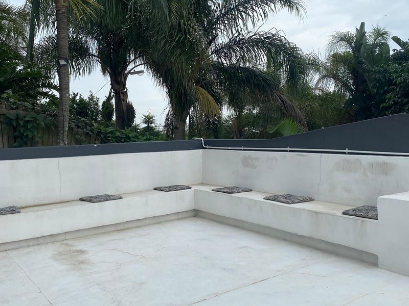 Outdoor patio area featuring built-in concrete bench seating and a boundary wall, set against a backdrop of mature garden trees.