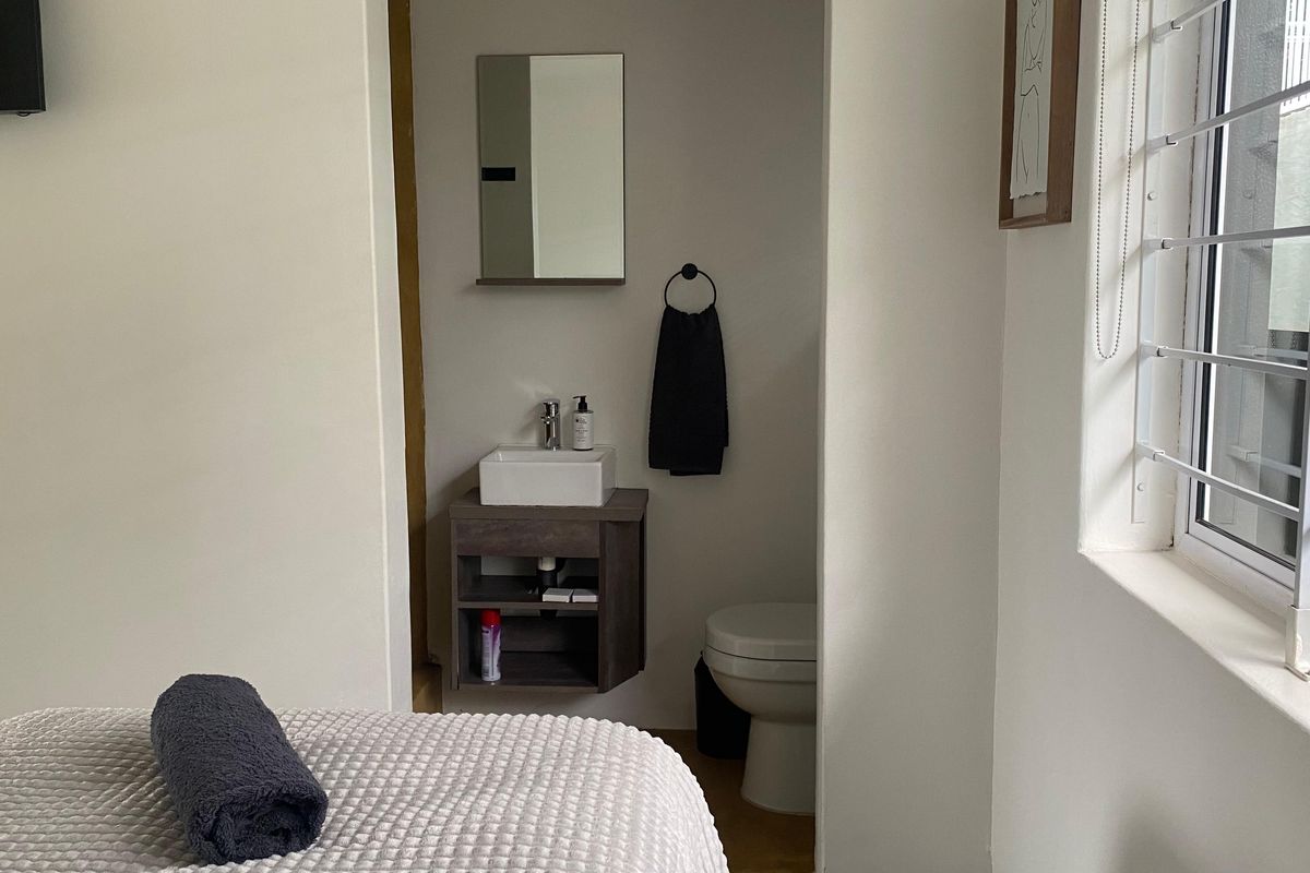 A compact en-suite bathroom featuring a modern wall-mounted vanity with a vessel sink, mirror, and toilet, situated adjacent to the bedroom area.
