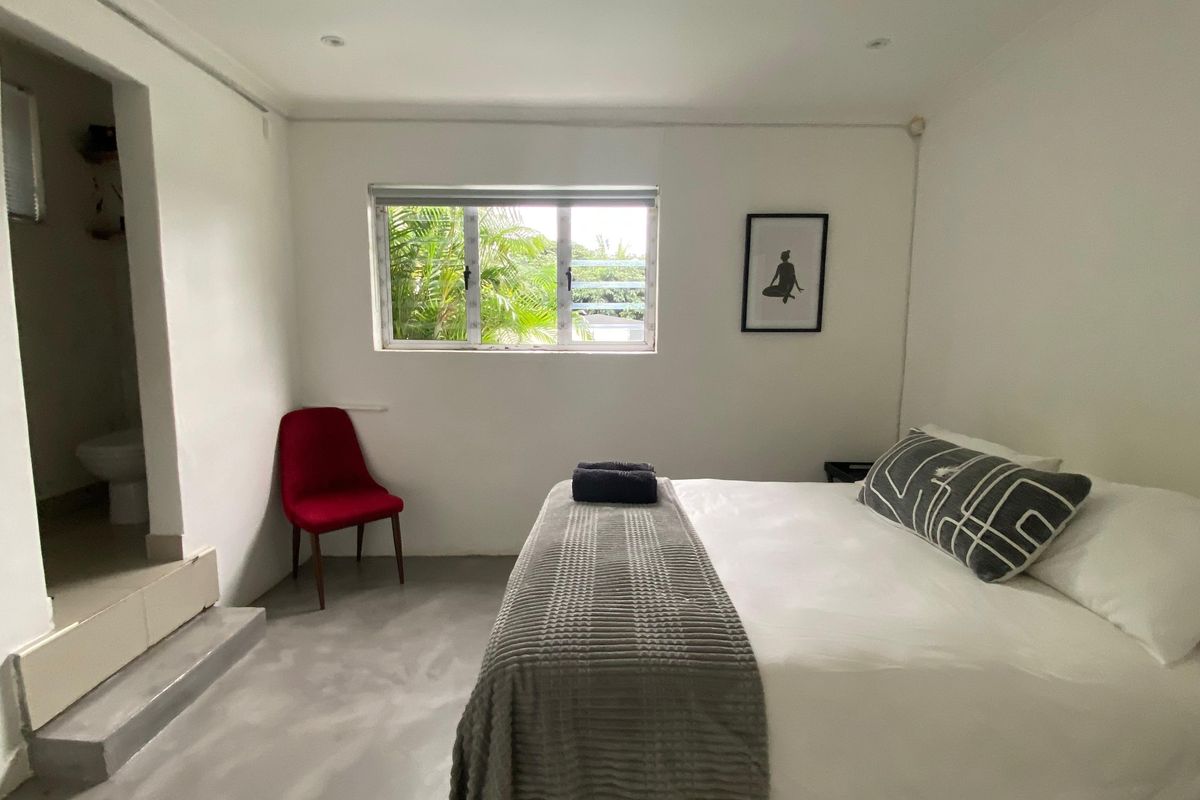 A bedroom featuring polished concrete flooring, recessed downlighting, and an en-suite bathroom access point with a step-up transition.