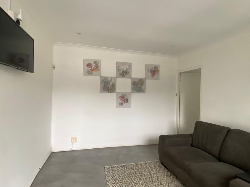 A simple living room featuring neutral walls, recessed downlighting, and polished concrete flooring.