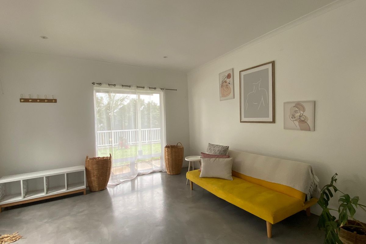A bright living room featuring polished concrete floors and a large sliding glass door providing access to the outdoor area.