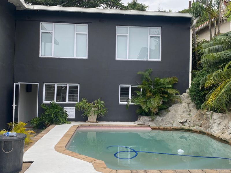 Rear exterior view featuring a swimming pool with a natural rock feature and dark-painted building facade with aluminium windows.
