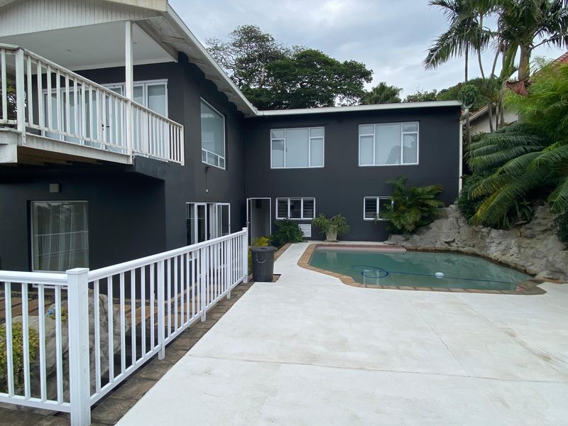 Rear exterior view featuring a swimming pool, concrete patio area, and a raised wooden deck with white balustrades.
