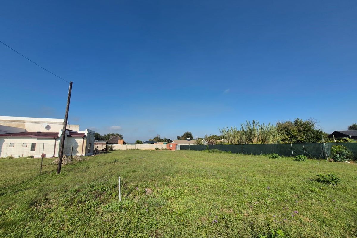A vacant residential plot featuring open grass, perimeter fencing, and a utility pole, offering a clear space for potential development.