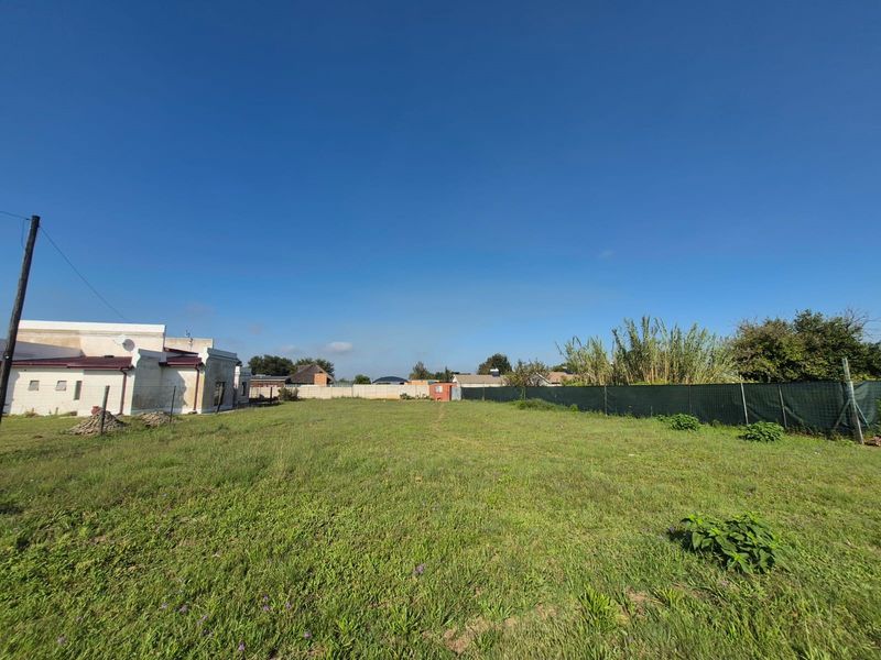 A wide, open residential plot featuring a grass lawn and perimeter fencing, offering a clear space for potential development.