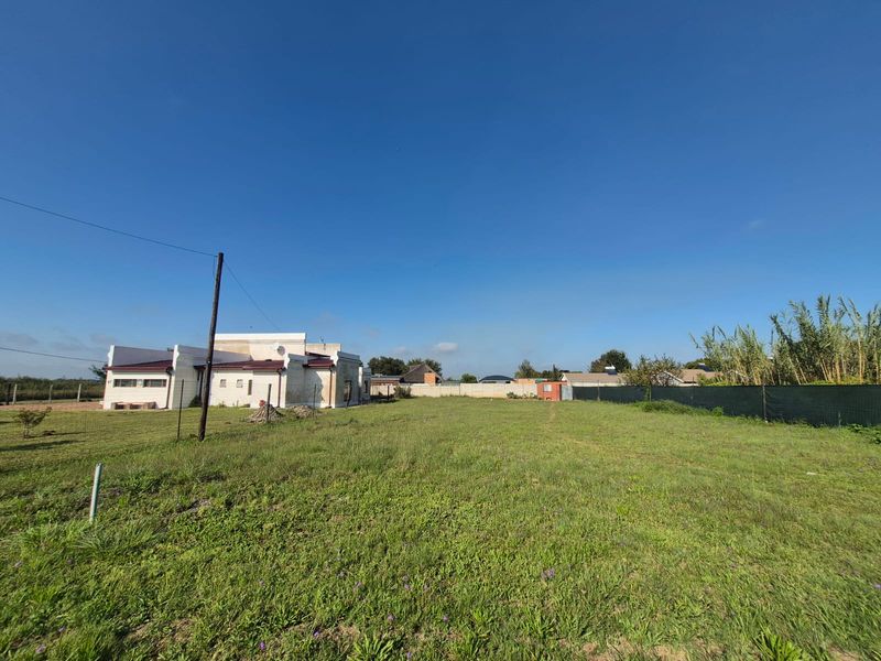 A spacious, level residential plot featuring a grass lawn, perimeter fencing, and a clear view of the adjacent property.