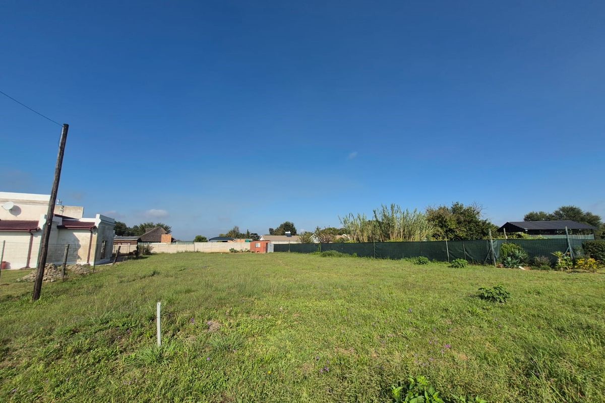 A vacant residential plot featuring open grass, perimeter fencing, and boundary walls, offering a clear space for potential development.
