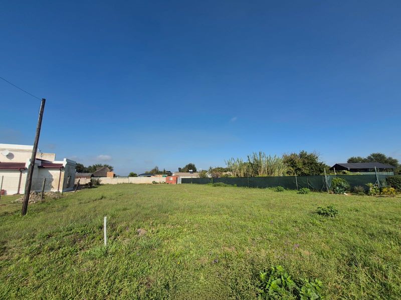 A vacant residential plot featuring open grass, perimeter fencing, and boundary walls, offering a clear space for potential development.