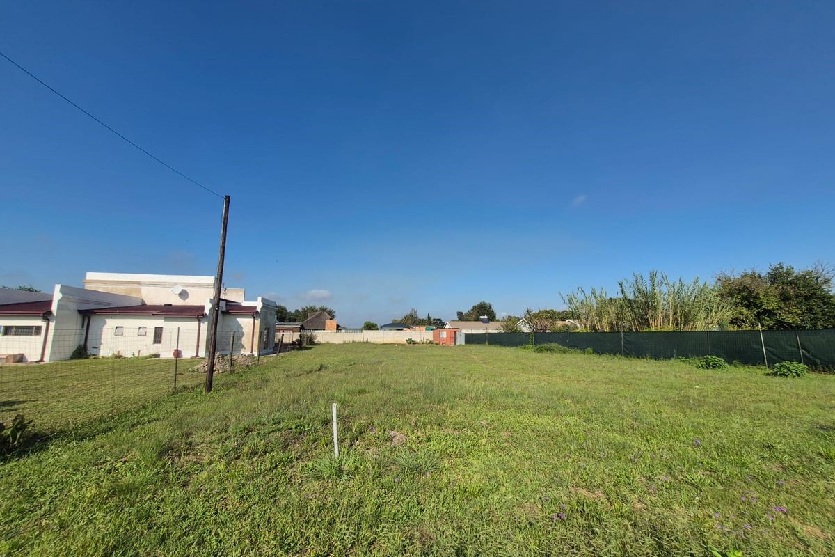 A spacious, level residential plot featuring a grass lawn, perimeter fencing, and an adjacent building structure.