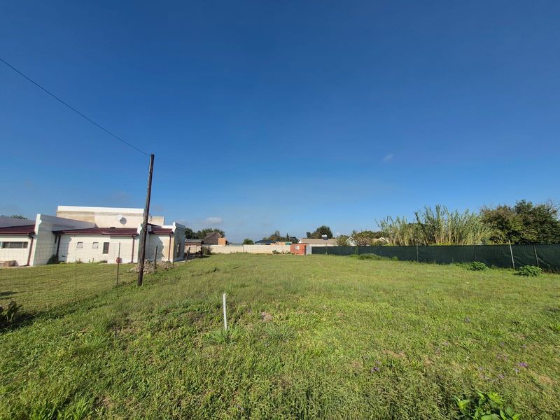 A spacious, level residential plot featuring a grass lawn, perimeter fencing, and an adjacent building structure.