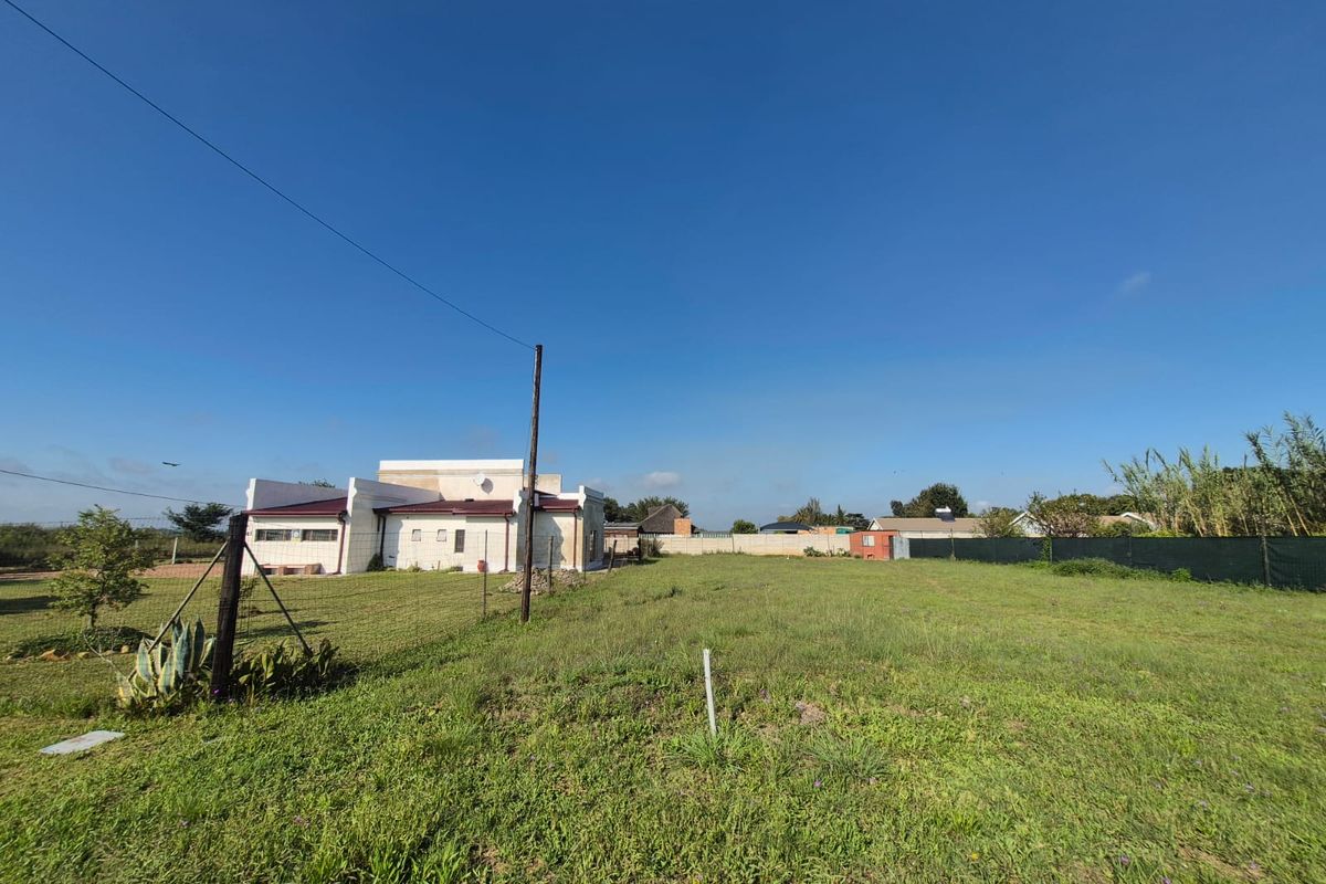A wide-angle view of a vacant residential plot featuring a grass lawn, perimeter fencing, and a utility pole with a neighboring structure visible.