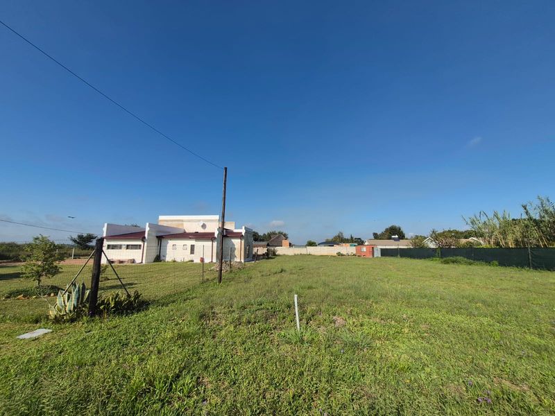 A wide-angle view of a vacant residential plot featuring a grass lawn, perimeter fencing, and a utility pole with a neighboring structure visible.