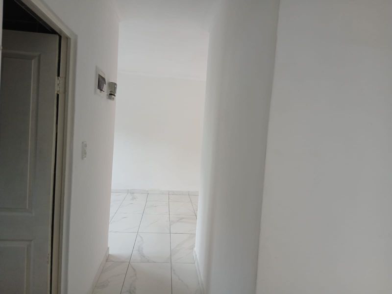 A clean, empty hallway featuring modern white marble-look floor tiles and neutral wall finishes, leading into an adjacent living space.