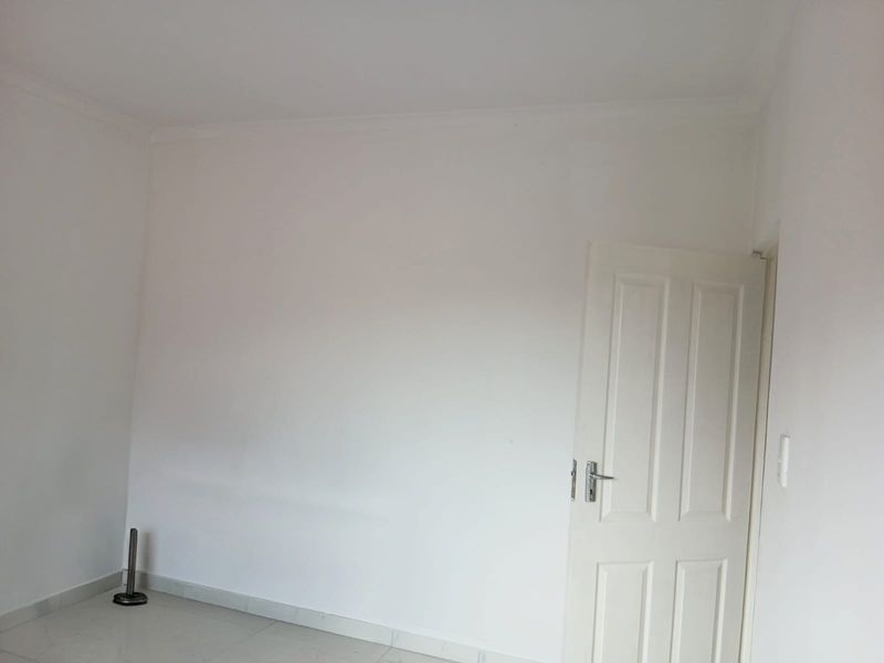 A clean, empty bedroom featuring neutral tiled flooring, white walls, and a classic panelled door, providing a blank canvas for interior design.