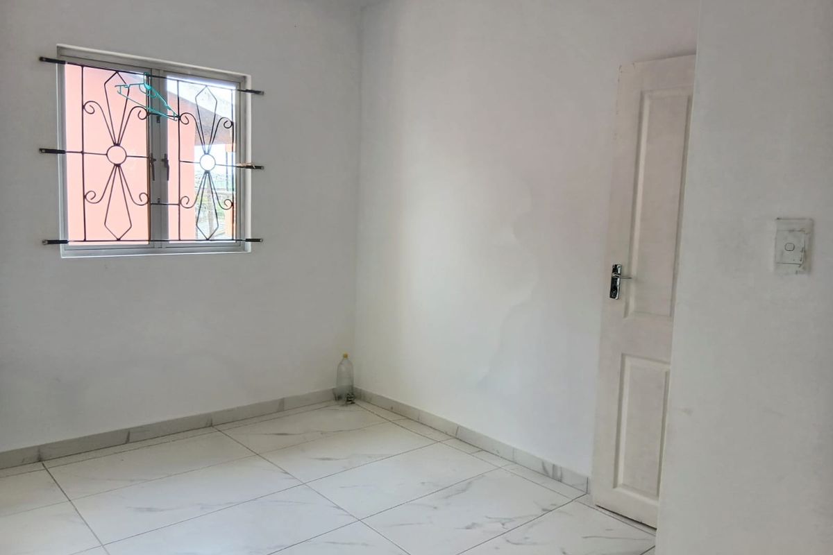 A vacant bedroom featuring white walls, tiled flooring, and a window with security bars. Visible water staining on the wall requires attention.