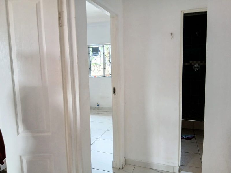A functional hallway connecting interior spaces, featuring tiled flooring and white painted walls, providing access to adjacent rooms.