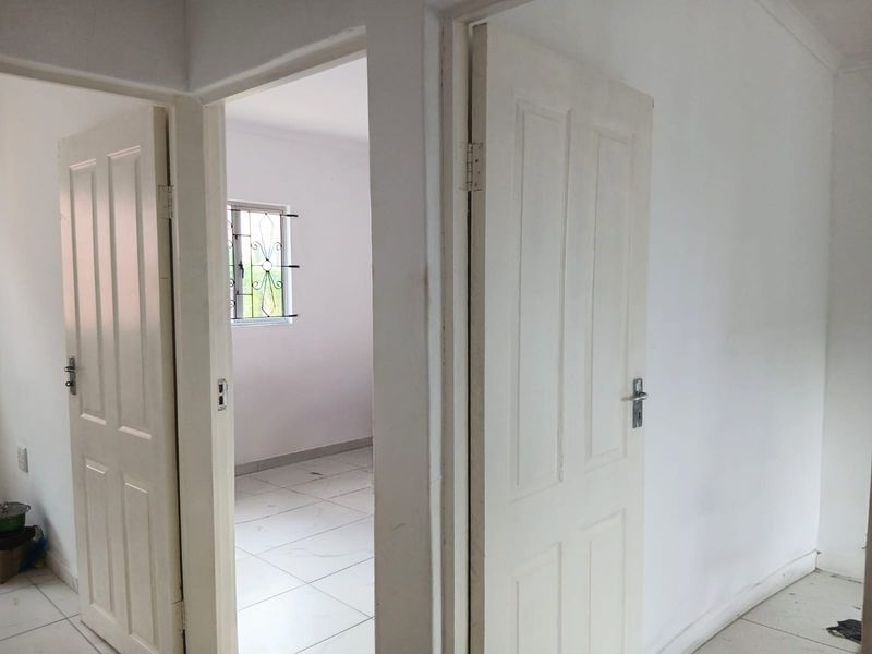 A bright, empty hallway featuring white tiled flooring and panel doors leading into adjacent rooms, providing a clean and neutral transition space.