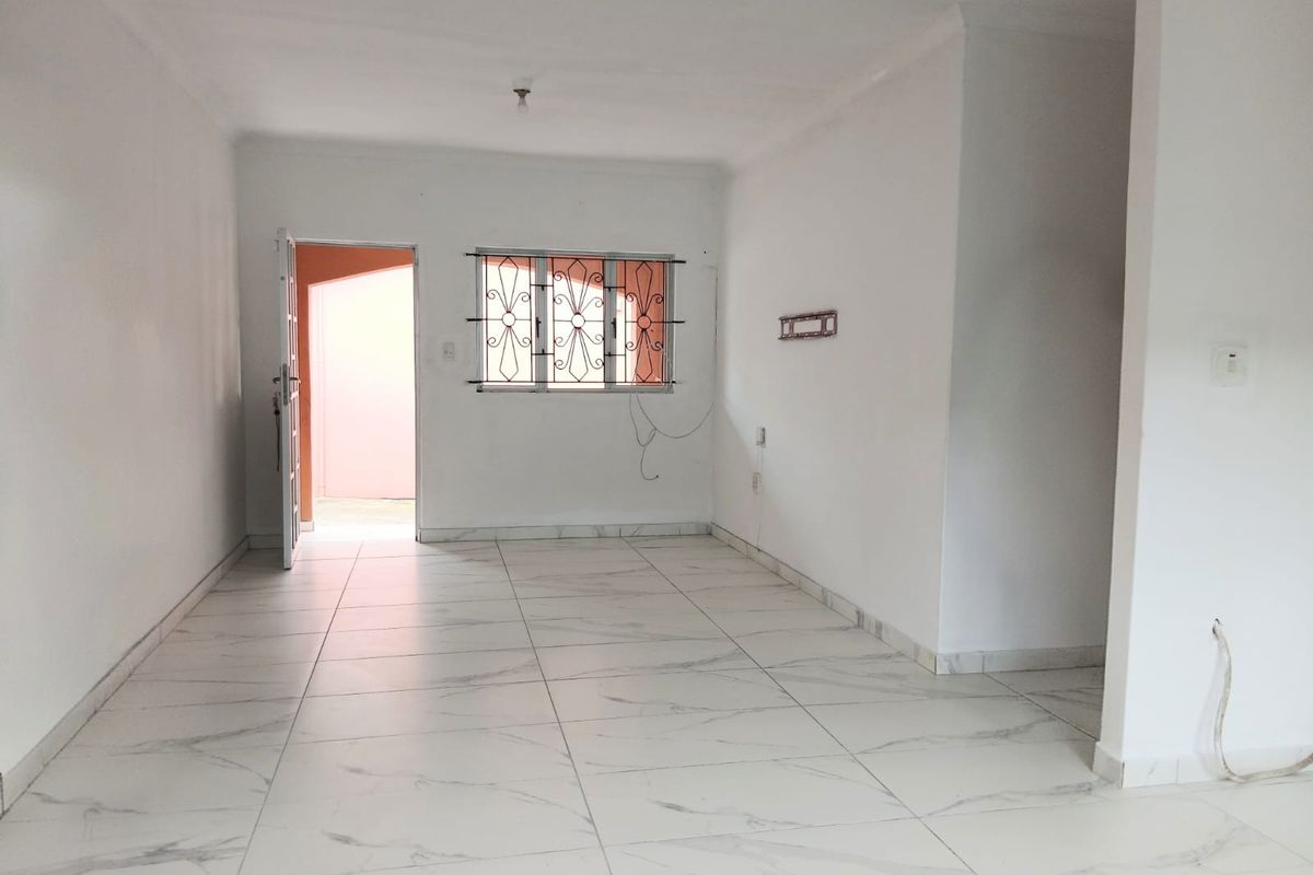 An empty, open-plan living area featuring white tiled flooring, neutral walls, and a window fitted with security bars.