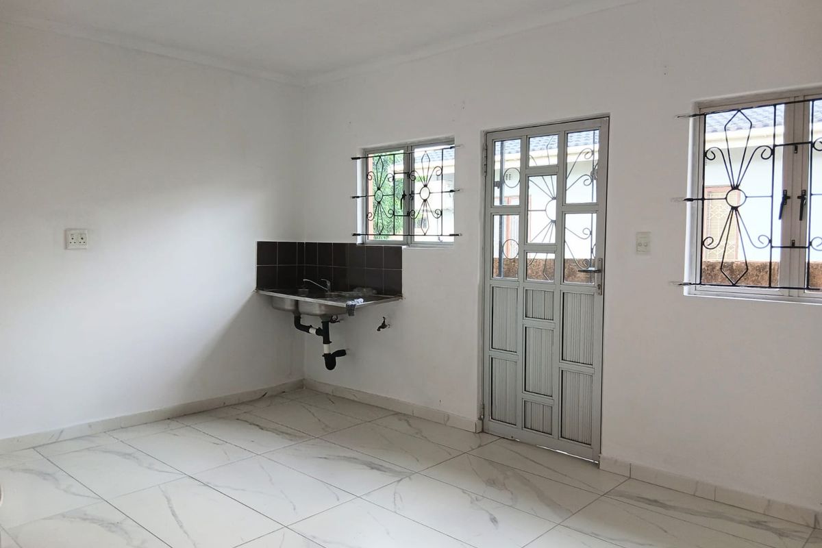 A minimalist kitchen area featuring marble-look floor tiles, a wall-mounted stainless steel sink with tiled splashback, and secure exterior access.