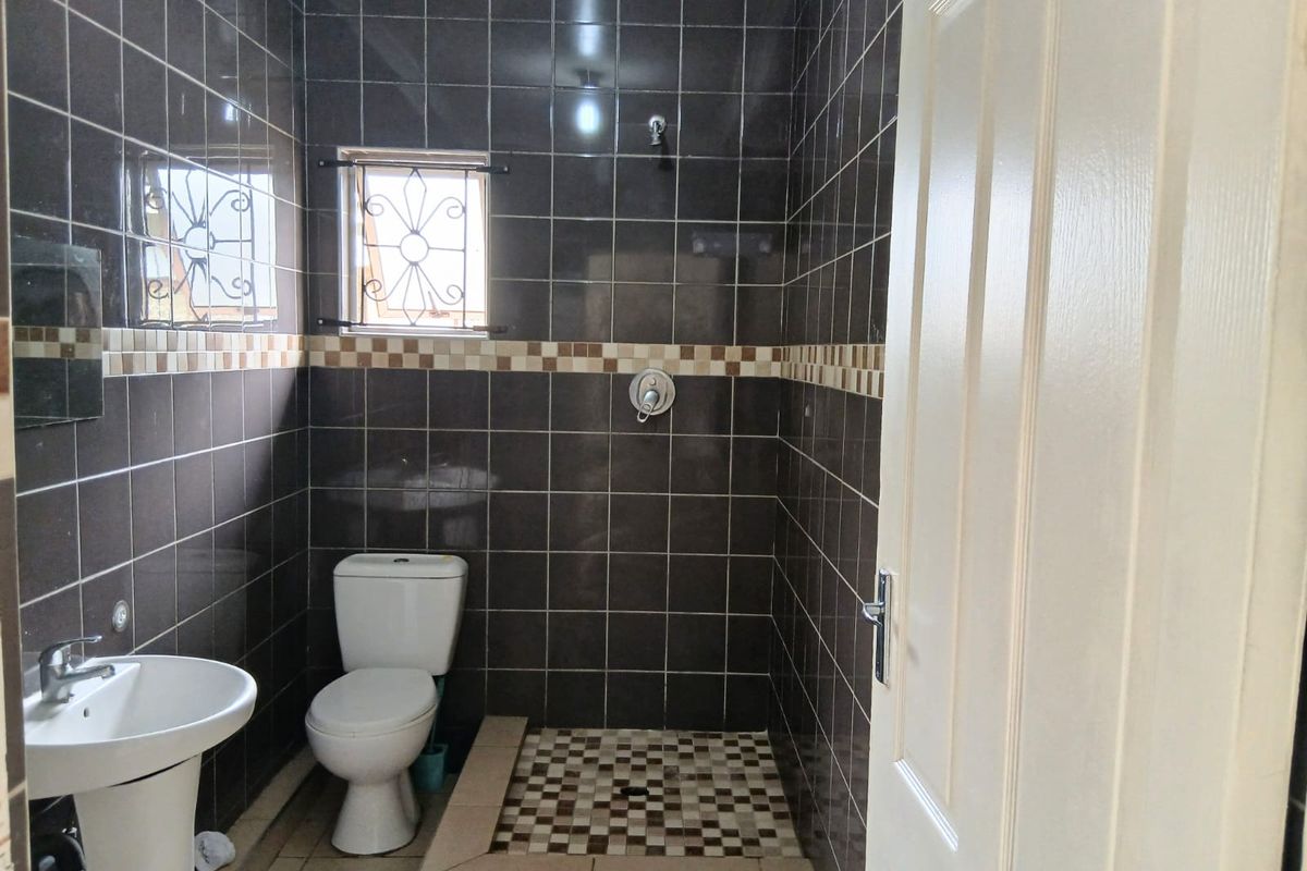 A functional bathroom featuring a pedestal basin, toilet, and a tiled walk-in shower area with dark wall tiles and decorative accents.