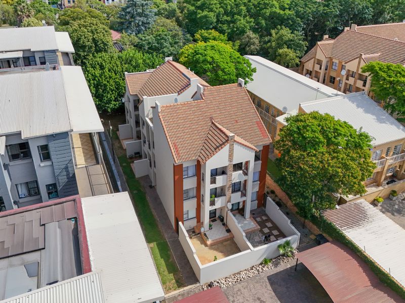 Aerial view of a multi-story apartment complex featuring terracotta tiled roofs, private ground-floor paved patios, and balconies within a landscaped residential setting.
