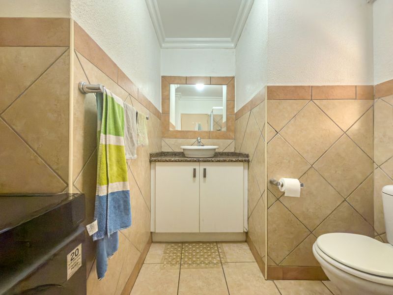 A functional bathroom featuring a vessel sink on a granite countertop, vanity cabinet, and neutral ceramic wall and floor tiling.