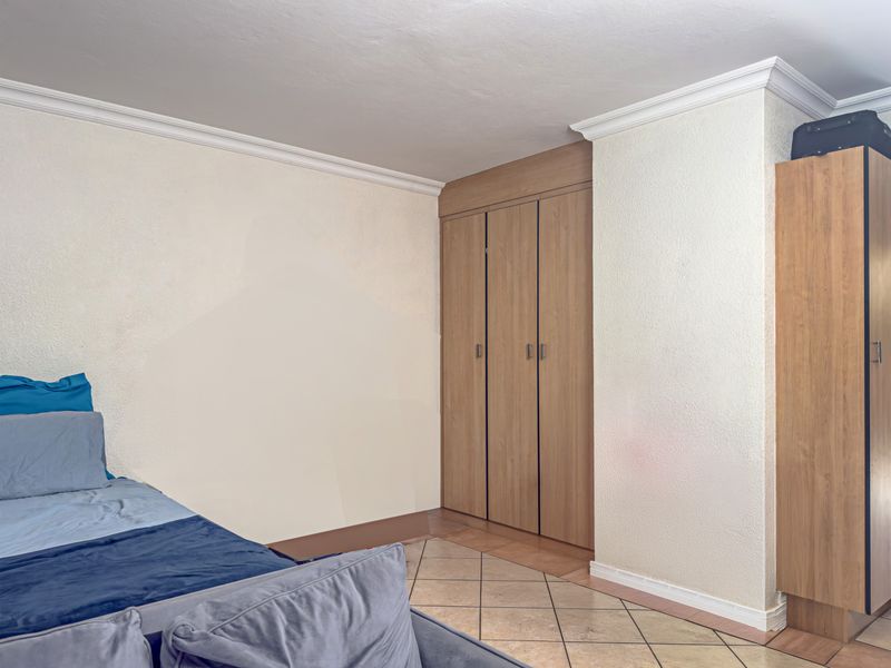Bedroom featuring built-in wooden wardrobes, crown molding, and tiled flooring. The walls show signs of uneven paint application.