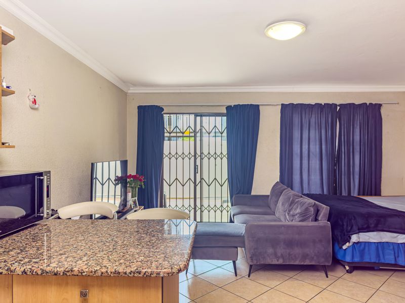 Open plan living area featuring a granite breakfast bar, ceramic tiled flooring, and a sliding glass door with security gate leading to the exterior.